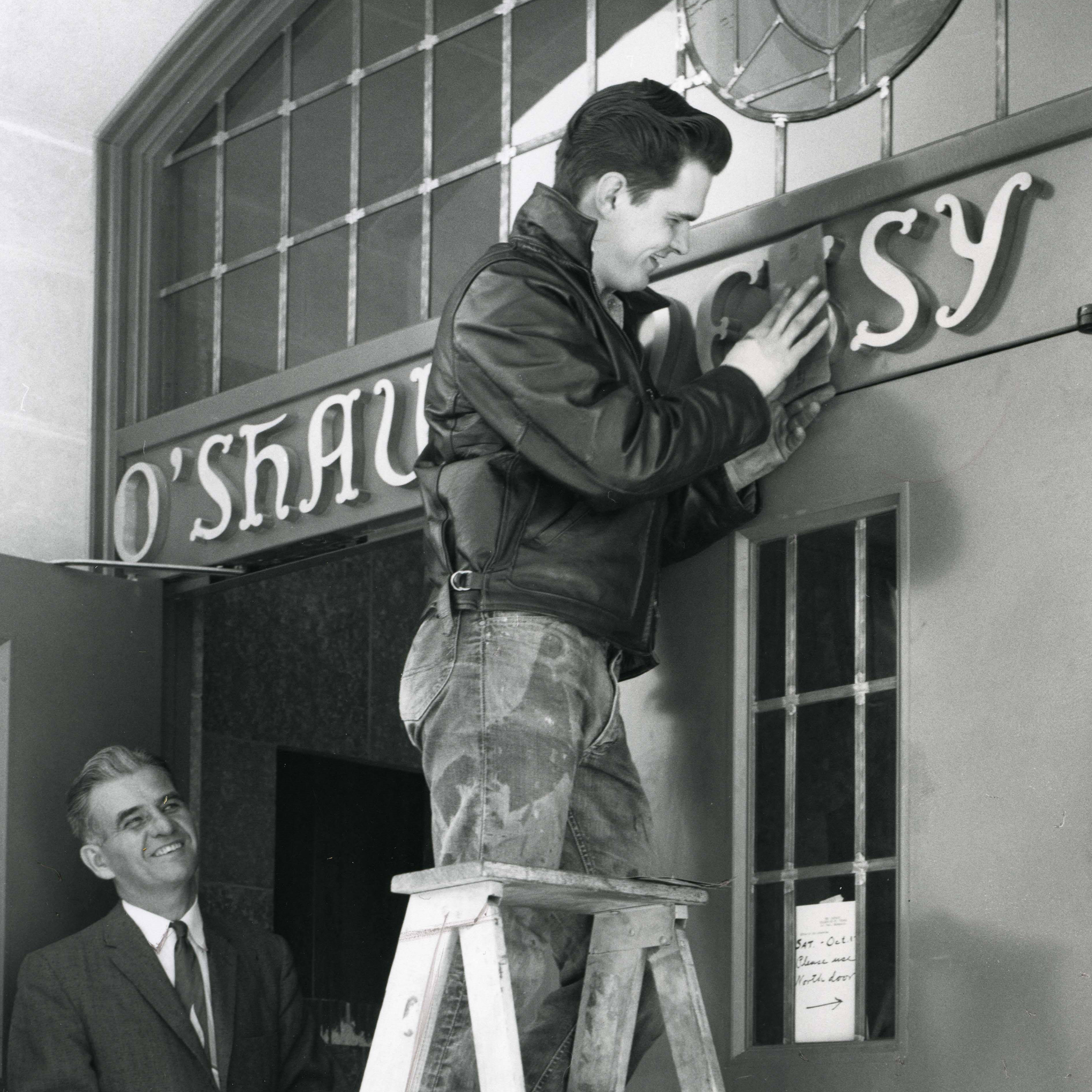 Archival photo of a man hanging the O’Shaughnessy signage