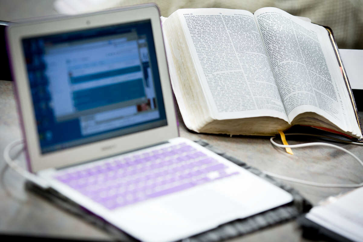 A laptop next to an opened Bible