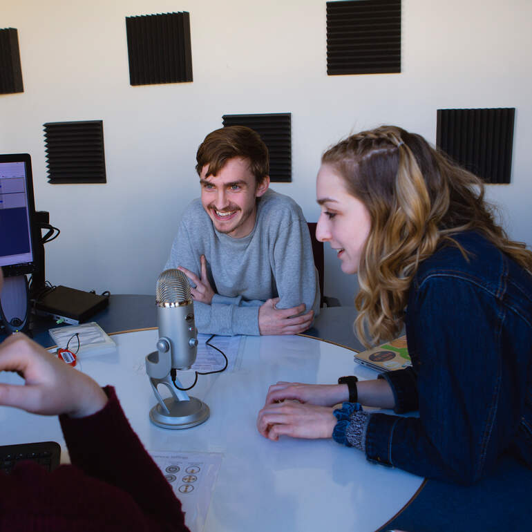 Students sitting around a table talking into a microphone